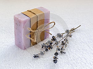 Purple soap bar with dry aromatic lavender flowers. Handmade soap on a white terry cotton towel. Natural toiletries and hygiene