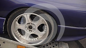 Purple sports car pulls off of the carrier trailer. Rear wheel close-up.