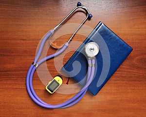 Purple stethoscope, notebook and portable pulse oximeter on a wooden background