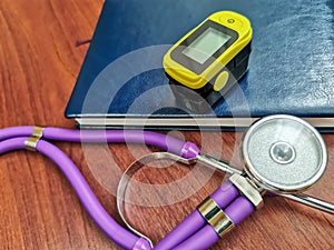 Purple stethoscope, notebook and portable pulse oximeter on a wooden background