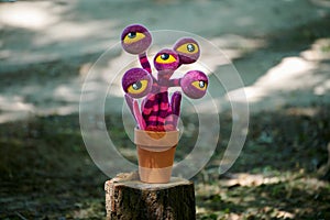 Purple striped flower with yellow eyes in clay pot on tree stump, strange crazy art object