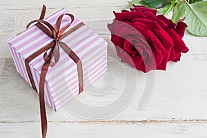 Purple striped gift box with brown ribbon bow and bautiful red rose on wooden background. Greeting card for holiday