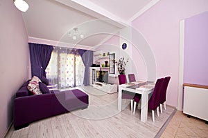 Purple studio apartment with a double sofa, a TV on the cabinet and a table with chairs