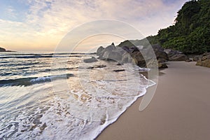 Purple sunrise in tropical beach, waves and stones on shore