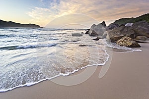 Purple sunrise in tropical beach, waves and stones on shore