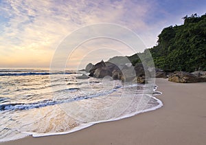 Purple sunrise in tropical beach, waves and stones on shore