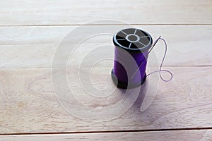 Purple thread spool and sewing needle with copy space isolated on wooden background closeup