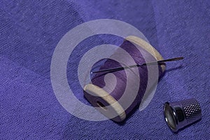 purple threads on a wooden spool with a needle on a background of lilac tulle, thimble