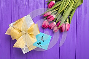 Purple tulip bouquet, blank greeting card for you and gift boxes. Top view over purple wooden table