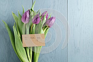 Purple tulips on blue wood background with i love you card top view