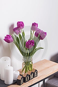 Purple tulips in a glass jar standing near thewall in the living room