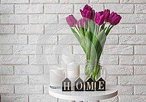 Purple tulips in a glass jar and wooden letters arranged into a word Home