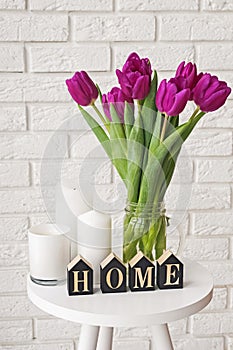 Purple tulips in a glass jar and wooden letters arranged into a word Home