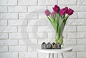 Purple tulips in a glass jar and wooden letters arranged into a word Home