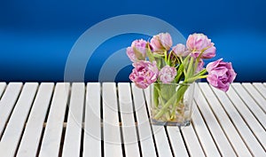 Purple tulips in the glass vase on the white wooden table and blue background