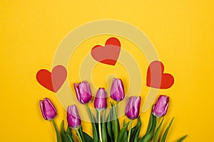 Purple tulips and three red crafted hearts over yellow background