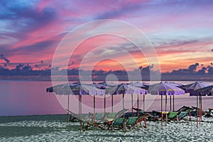 Purple umbrella and green chairs in morning beach, sunrise shot