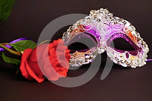 Purple Venetian carnival mask, red rose. Black background.