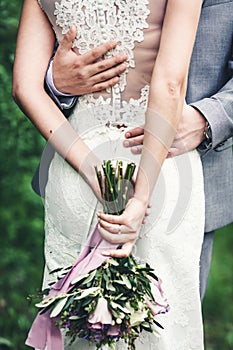 Purple wedding bouquet in the hands of the bride. The guy is hugging the girl. Back view