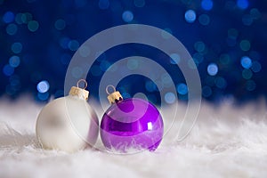 Purple and white Christmas balls on fur with garland lights on b