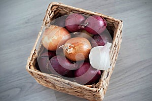 Purple and white onions in squar, wicker box on the wooden background photo