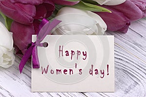 Purple and white tulips with white paper on a white wooden background and card lettering happy women`s day english. Womans Day. 8