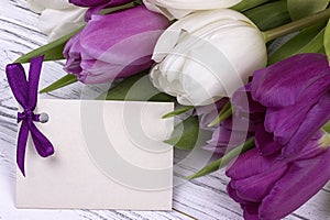 Purple and white tulips with white paper on a white wooden background with card for text. Womans Day. 8 March. Mother`s Day.