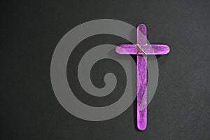 A purple wooden cross in black background. Christian faith, holy week or lent season celebration concept.