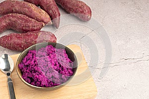 Purple yams pile and mashed potatoes on a dish on a gray stone background.