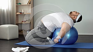 Purposeful overweight male lifting dumbbells lying on fitness ball, muscles pump