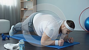 Purposeful overweight man doing plank exercise at home, desire to lose weight