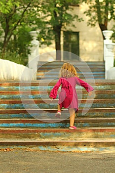 Purposeful toddler girl in pink dress reaching the top of old blue vintage stairs