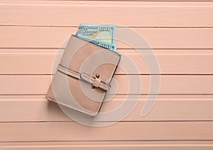 A purse with dollar bills on a pink wooden table. Top view