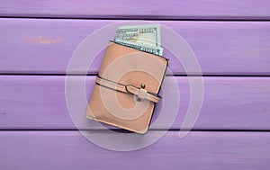 A purse with dollar bills on a pink wooden table. Top view