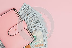 Purse with one hundred dollars banknotes on pink background. Flat lay, top view, copy space