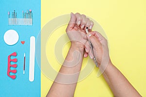 Push back the cuticle with a metal pusher. Home nail care, beauty. Health concept. Yellow and blue background.