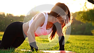 Push ups or press ups exercise by young woman. Girl working out on grass crossfit strength training in the glow of the