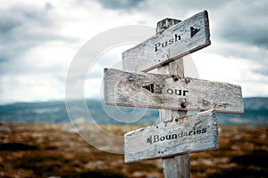 Push your boundaries text on wooden rustic signpost outdoors in nature/mountain scenery.
