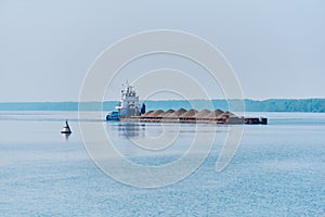 Pusher tug pushes dry bulk cargo barge with sand on the river in the morning haze