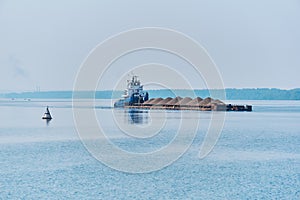 Pusher tug pushes dry bulk cargo barge with sand on the river in the morning haze