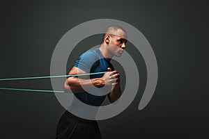 Pushing hard. Sportsman working out with resistance band over dark background