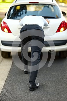 Pushing his car onto the curb. Rear view of a man pushing his car.