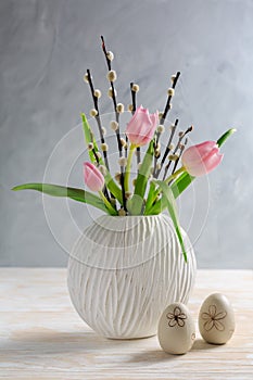 Pussy willow branches with tulips in vase with Easter egg on wooden kitche table