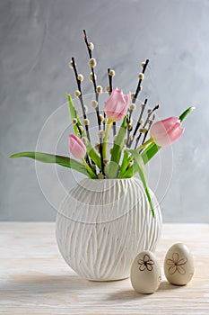 Pussy willow branches with tulips in vase with Easter egg on wooden kitche table photo