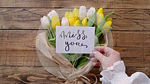 Put a card MISS YOU on a tulipâ€™s bouquet on a wooden table top view