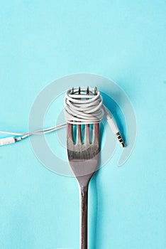 Put the soul into your food. Studio shot of earphones wrapped around a fork against a blue background.