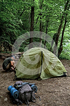 Put tourist tent in campsite and prepare for rest. Young handsome Caucasian male traveler with bandana on his head and beard sets