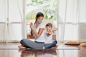 Put your hands together. a cheerful young mother and daughter doing a yoga pose together while being seated against each