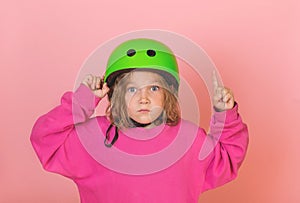 Put on your helmet. Safety and protection. Little cute kid girl in green bike helmet pointing finger up with successful