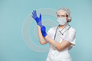 Puts on blue gloves. Doctor or nurse woman in a personal protective suit with a stethoscope, on a blue background. In a